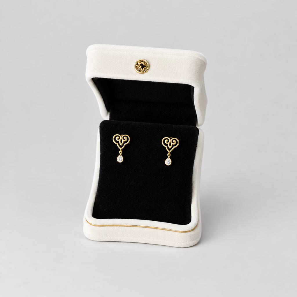A pair of gold heart-shaped dangle earrings displayed in an open white jewelry box with a black velvet interior, set against a split black and white background.