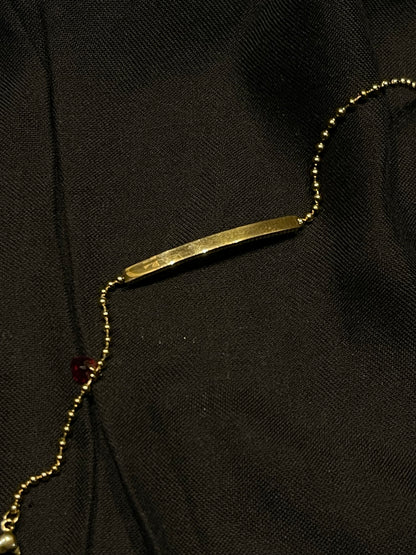 A gold bar necklace with a matching gold beaded chain, laid out on a textured black fabric background.