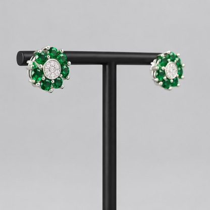 A pair of floral cluster stud earrings with green gemstones and a central clear stone, displayed on a black T-stand against a light gray background.