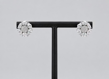 A pair of silver-toned cluster stud earrings with clear gemstones, displayed on a black T-stand against a light gray background.