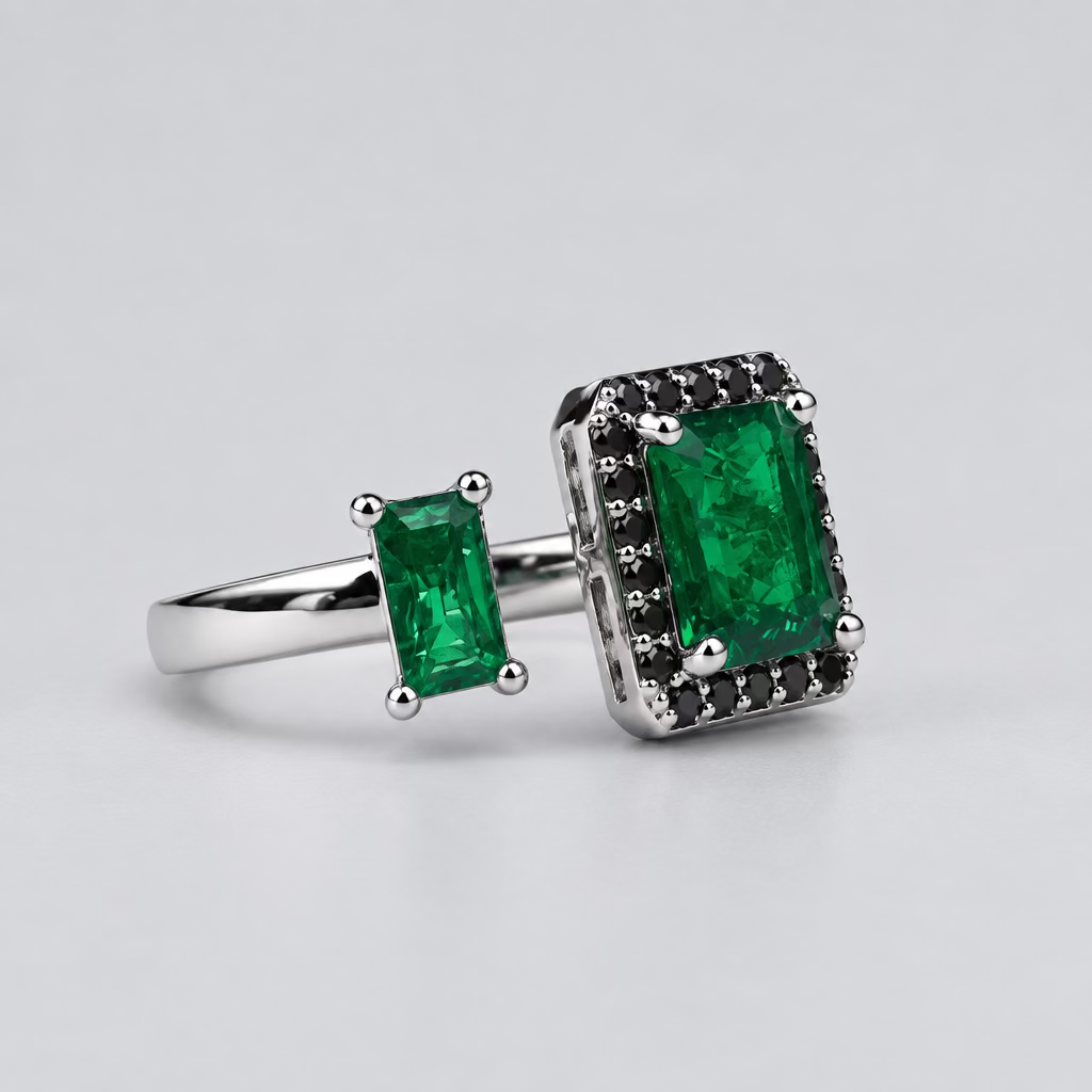 A silver ring featuring a large rectangular green emerald-cut center stone and a smaller matching green stone on the band, displayed in front of a blurred white jewelry box with an orange logo.