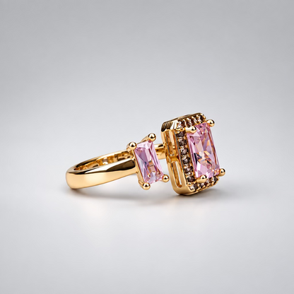 A rose gold ring with a rectangular pink gemstone and a smaller pink baguette stone, displayed in front of its white Meenu jewelry box on a light purple surface.