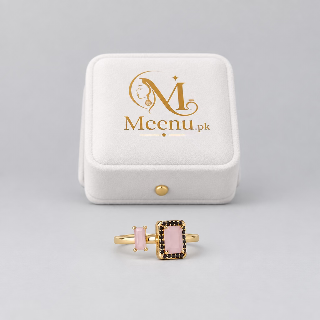 A rose gold ring with a rectangular pink stone and black accent stones, displayed in front of its white Meenu Jewels box on a light purple surface.