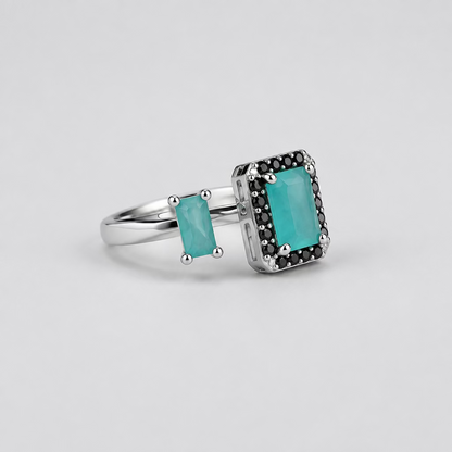 A silver ring with a rectangular turquoise stone and small side stones, displayed in front of its white Meenu.pk branded jewelry box on a light surface against a dark background.