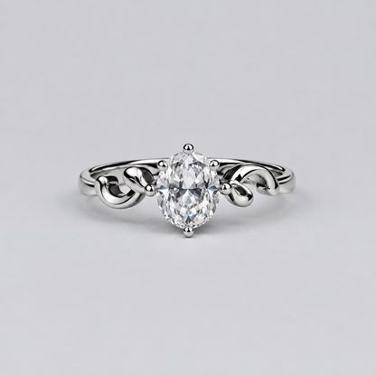 A silver ring with a heart-shaped clear gemstone is displayed in the foreground on a light surface, with a white jewelry box branded 'Meenu' in the blurred background against a dark backdrop.