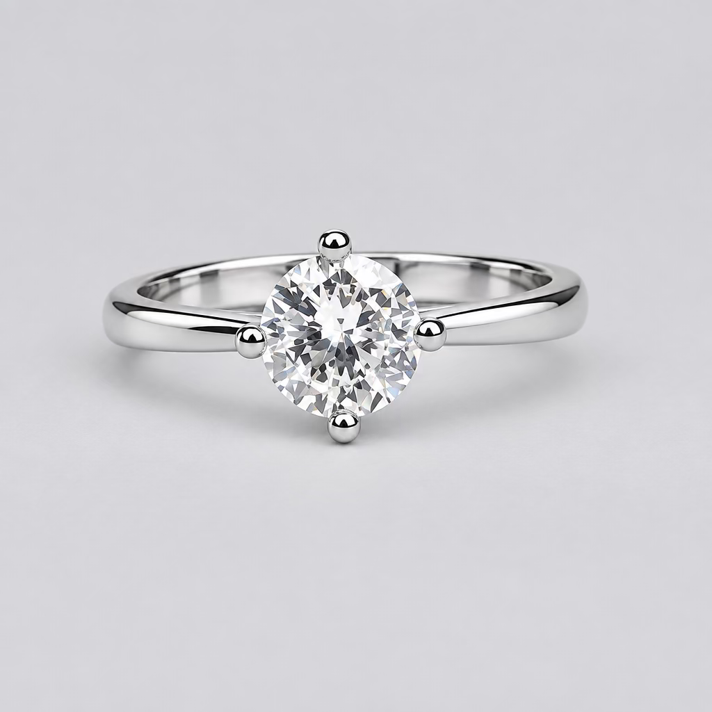 A silver solitaire ring with a clear round gemstone is displayed on a light surface, with a blurred white jewelry box featuring an orange 'M' logo in the background.