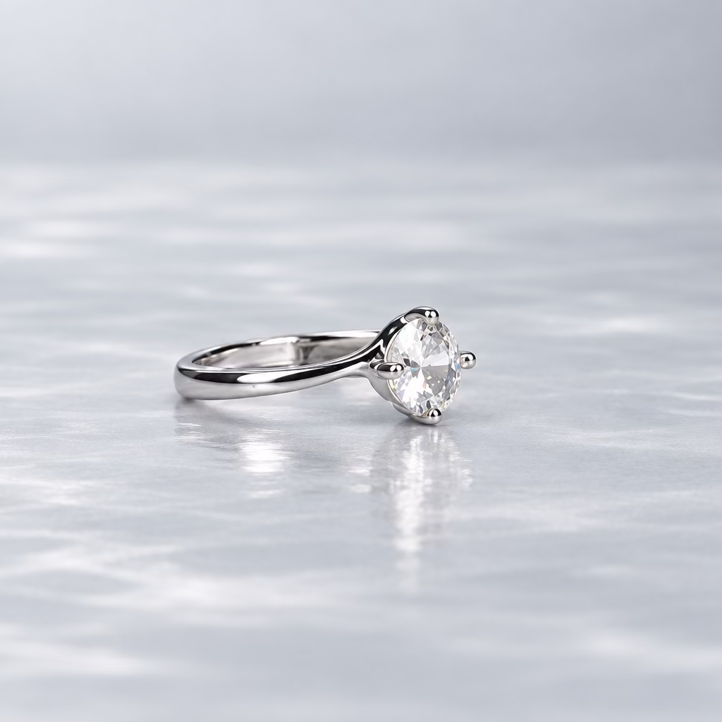 A silver ring with a clear gemstone is displayed on a light lavender surface, with its branded white presentation box in the background against a dark gray backdrop.