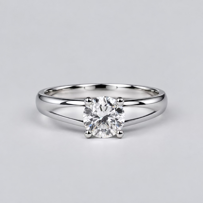A silver ring with a clear central gemstone is displayed on a light surface, with a white Meenu jewelry box in the blurred background.