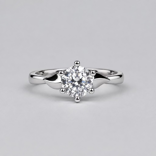 A silver engagement ring with a clear round-cut center stone is displayed on a light surface, with a white Meenu jewelry box in the blurred background.