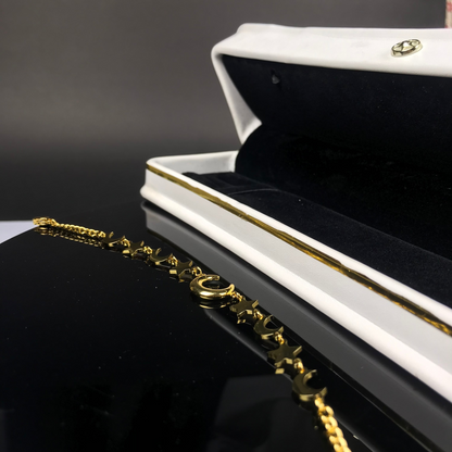 A gold-tone chain bracelet with a circular charm, displayed on a glossy black surface next to an open white jewelry box with gold trim.