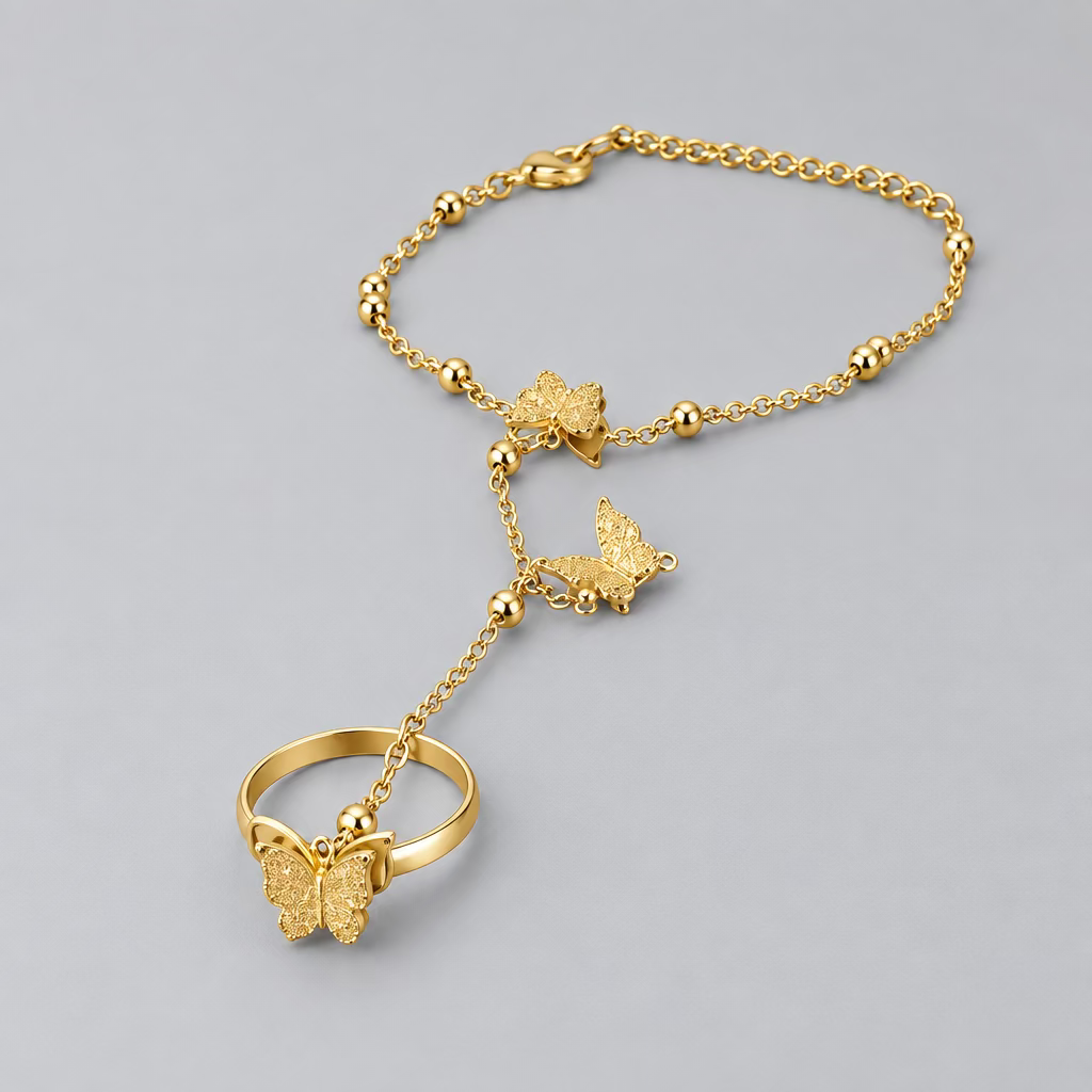 A gold-toned chain bracelet with butterfly and heart charms, displayed on a black circular surface against a dark background.