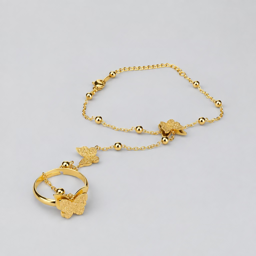 A gold-toned beaded chain bracelet with butterfly and flower charms, displayed on a clean light gray background.