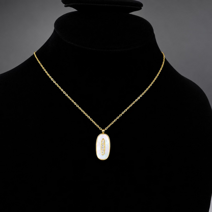 A gold chain necklace with an oval pendant featuring a white iridescent center and a small gold feather motif, displayed on a black velvet jewelry bust.