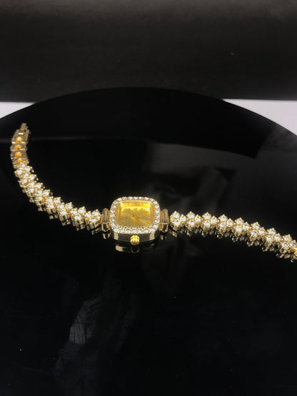 A yellow gold watch with a square bezel and a diamond-encrusted bracelet, displayed on a black surface.