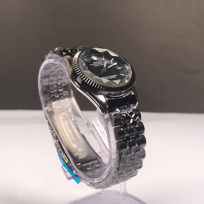 A stainless steel wristwatch with a black dial and matching black metal bracelet, displayed on a clear plastic stand against a neutral gray and white background.