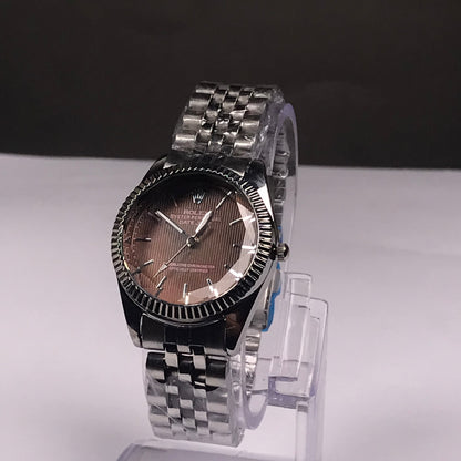 A Rolex wristwatch with a stainless steel Oyster bracelet and a rose gold-toned dial, displayed on a clear stand against a split white and dark gray background.