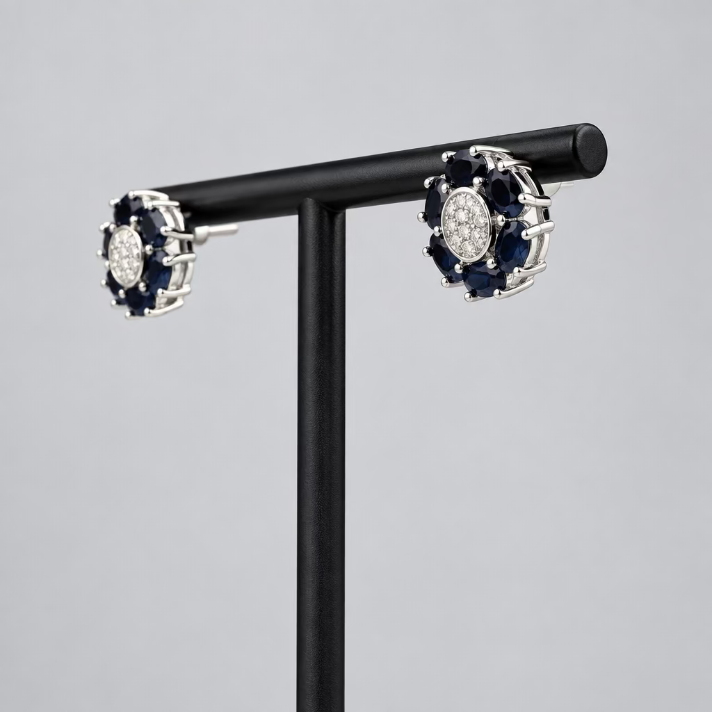 A pair of round cluster stud earrings with dark blue stones and a central clear stone, set in silver-toned metal, displayed on a black T-stand against a light gray background.
