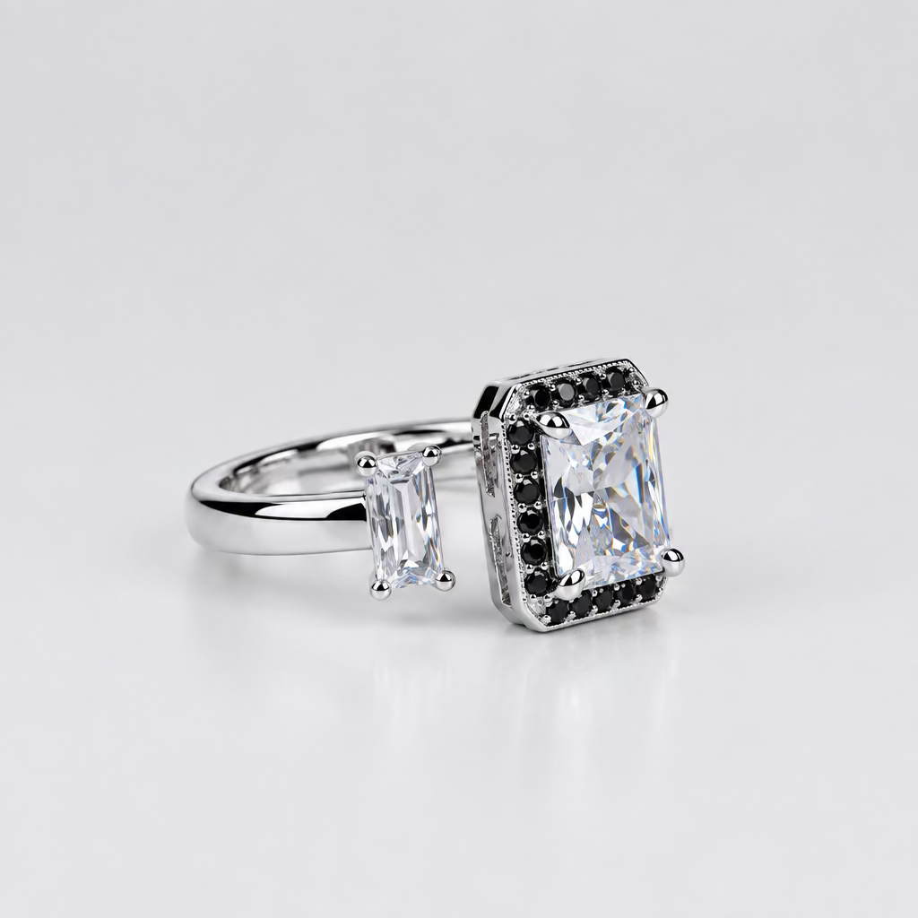 A silver-toned ring with a large rectangular clear gemstone and smaller side stones, displayed on a light surface with a blurred white jewelry box in the background.