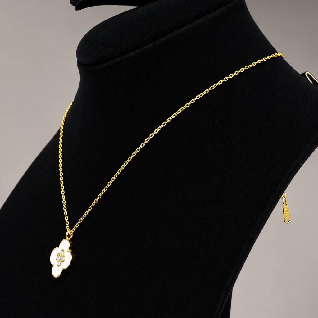 A gold chain necklace with a white enamel pendant featuring a gold monogram, displayed on a black velvet jewelry bust.
