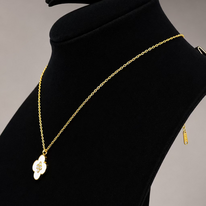 A gold chain necklace with a white enamel pendant featuring a gold monogram, displayed on a black velvet jewelry bust.
