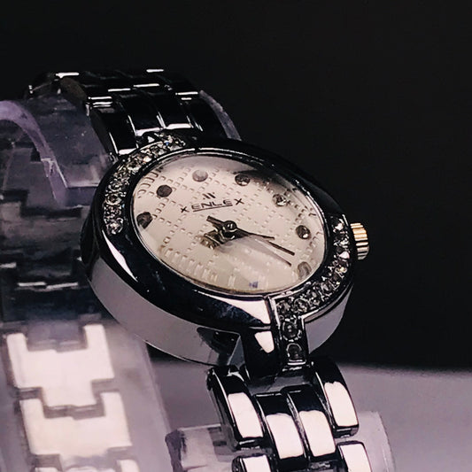 A close-up shot of a Kenlex women's watch featuring a silver-tone metal bracelet, a white textured dial, and a bezel set with small clear crystals.