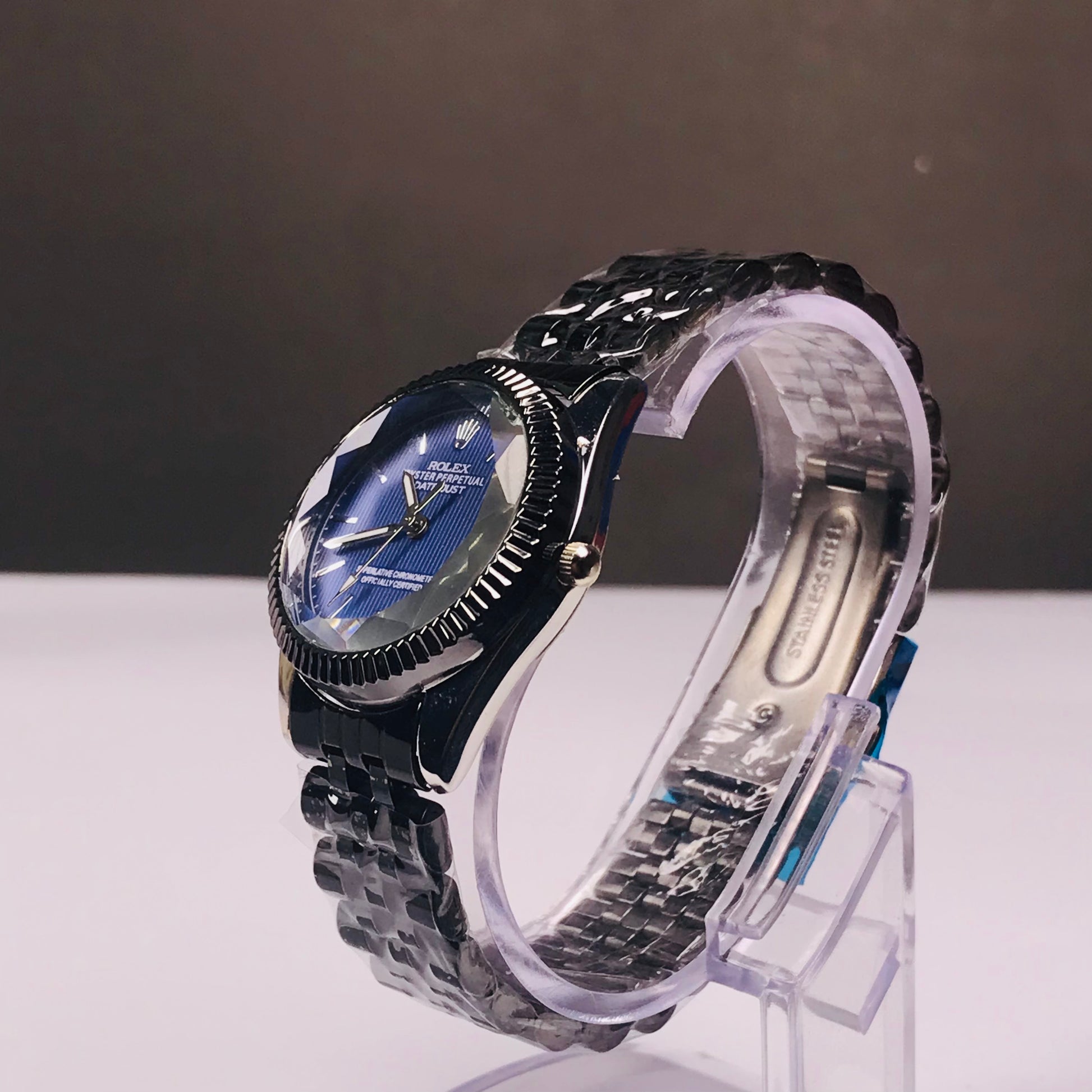 A wristwatch with a dark blue dial and a silver-toned metal link bracelet, displayed on a clear stand against a dark gray background.
