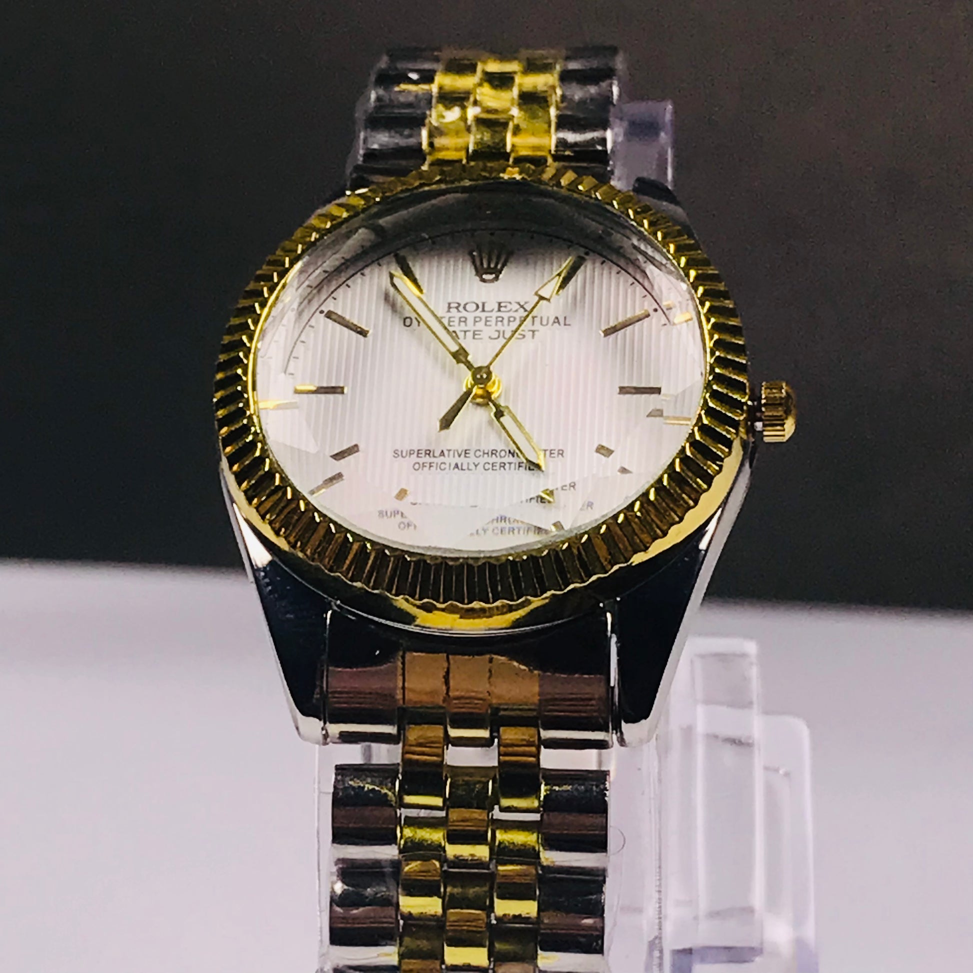 A Rolex wristwatch with a two-tone yellow gold and stainless steel link bracelet, a fluted gold bezel, and a white dial with gold hands and markers, displayed on a clear stand.