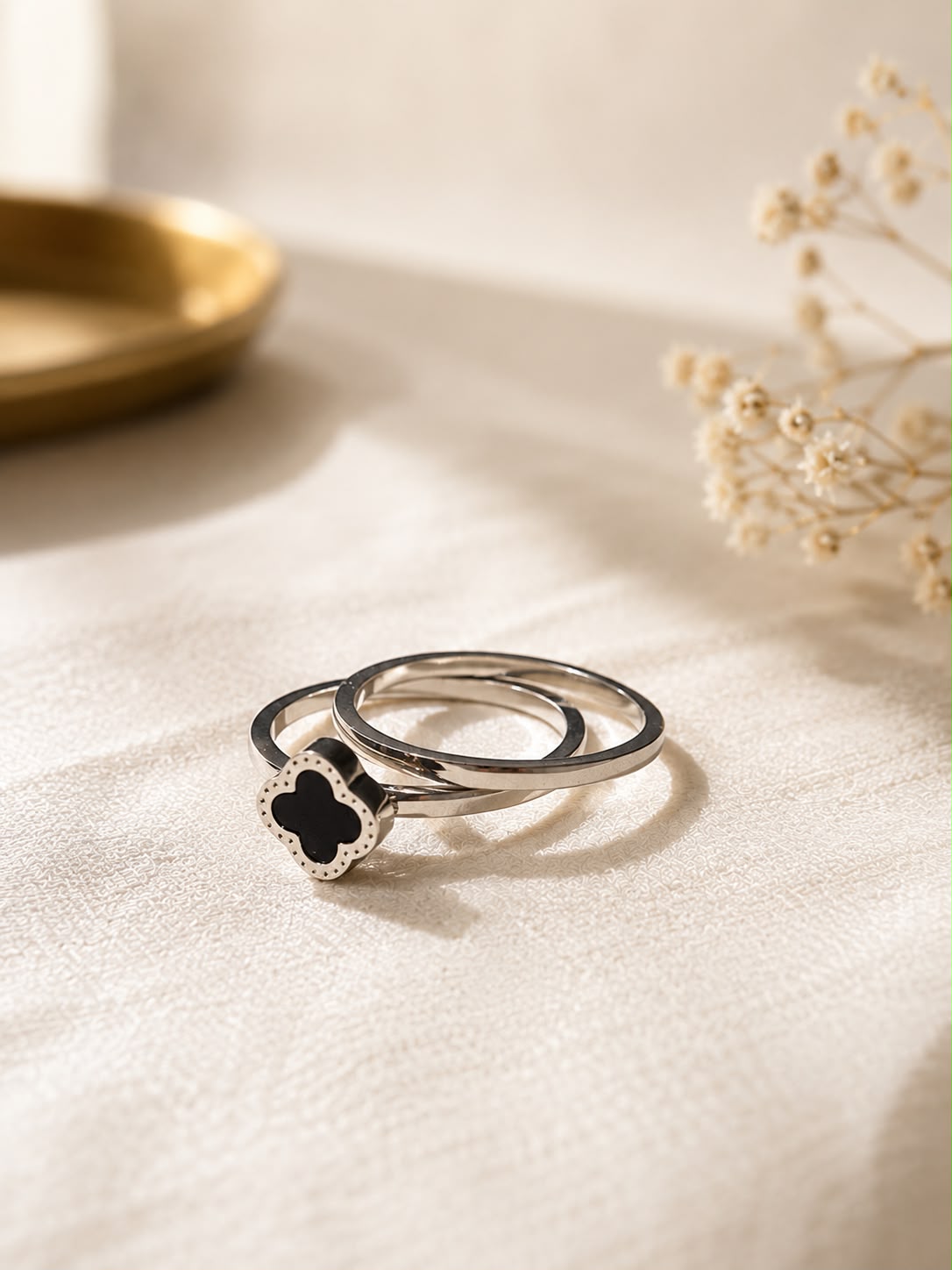 Two silver rings on a textured cream fabric background, with one ring featuring a black clover-shaped stone surrounded by a small silver border.